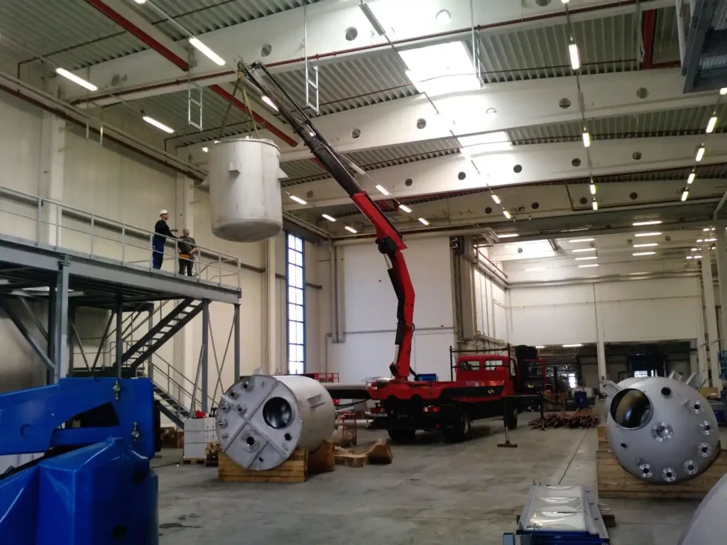 Ein Kran hebt einen großen Behälter in einer Industriehalle.