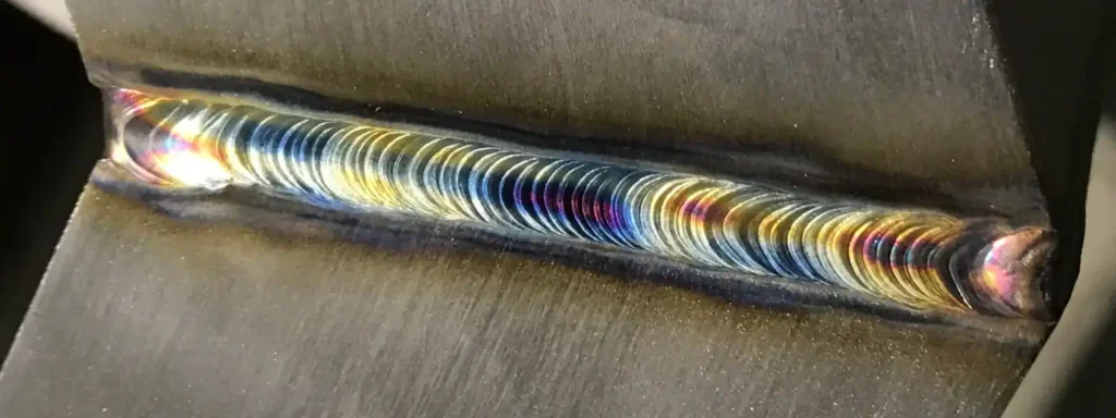 Detailaufnahme einer farbigen Schweißnaht auf Metalloberfläche.