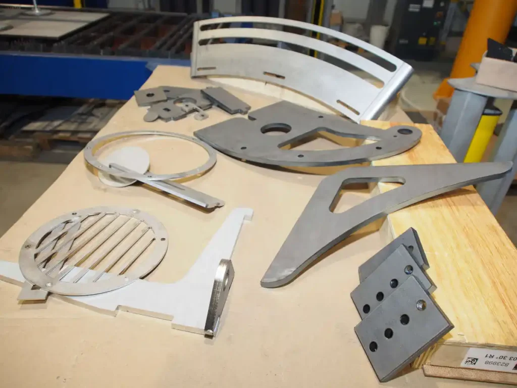 Verschiedene CNC-Laserschnittteile aus Edelstahl und Aluminium auf einer Arbeitsfläche.