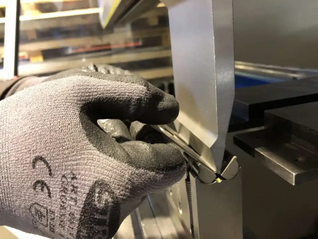 Hand mit schwarzem Handschuh, die ein Werkstück beim Abkanten hält.