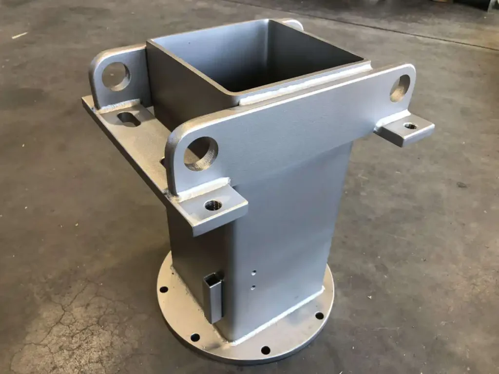 Metallische Schweißbaugruppe mit quadratischem Ausschnitt und Befestigungslöchern.